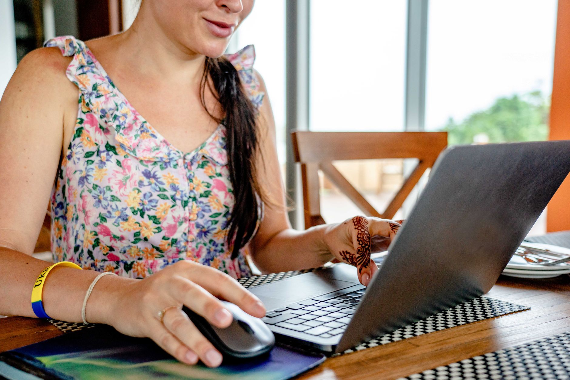 A woman using a laptop for remote work indoors, featuring a floral dress and henna design.